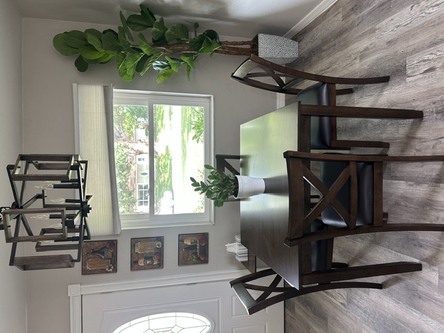 Dining area with a dark wood table and four chairs beneath a modern chandelier, next to a bright window and a tall plant