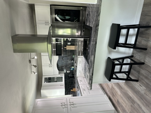 Full kitchen with white cabinets, granite breakfast bar with two stools, and stainless steel appliances