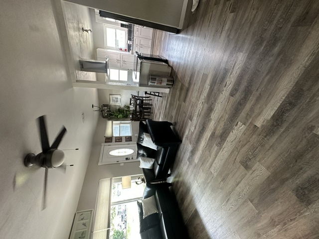 The open, comfortable shared living room at The Warriors Landing, with sofas and wood-look flooring opening toward the kitchen