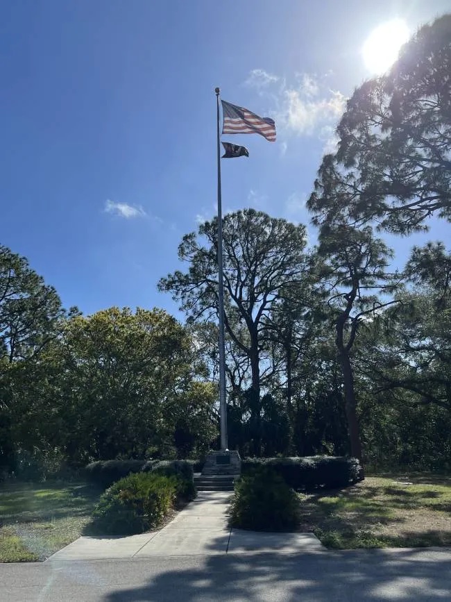 A restored green military tank displayed behind a low fence among trees at a veterans memorial park